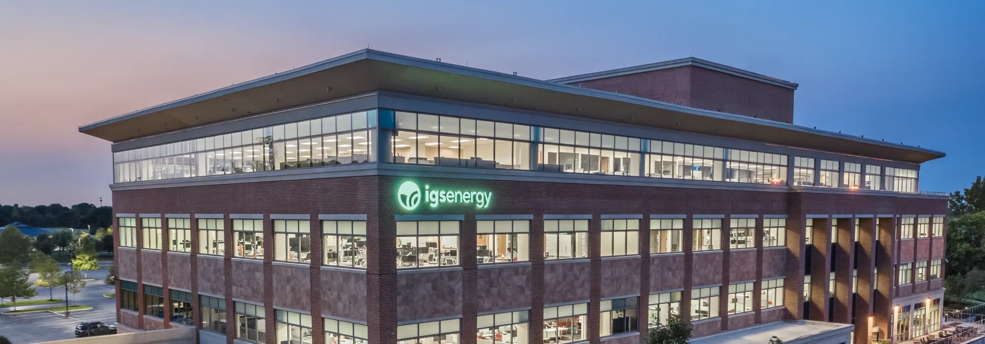 The lit headquarters at dusk, seen from the air, the illuminated mark carried across the third floor