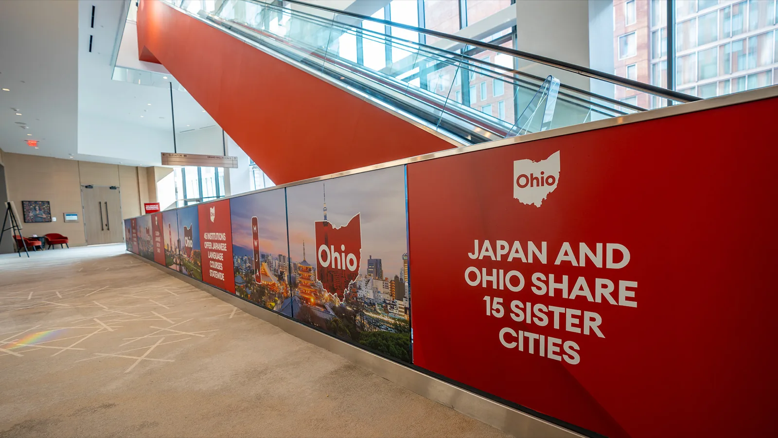 A stair wall reading “Japan and Ohio share 15 sister cities”, escalators crossing above it
